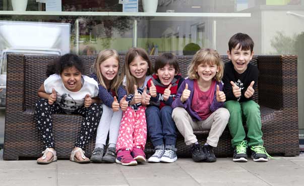 A couple of children are sitting in front of a builduing and are giving a thumbs up.